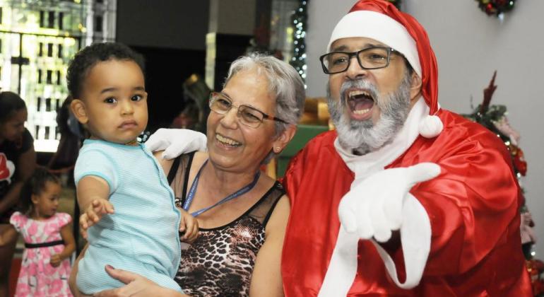 Papai Noel ao lado de uma senhora com uma criança no colo