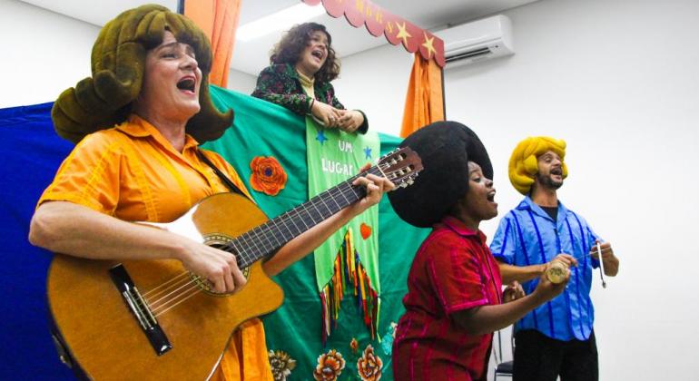 Quatro atores realizam um apresentação musical. 