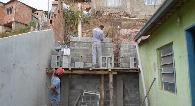 Dois trabalhadores constroem um muro em frente a um barranco. 