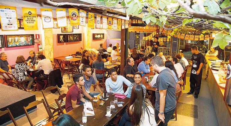 Cerca de 30 jovens e adultos bebem cerveja e conversam em mesas de bar à tarde. Foto: Divulgação