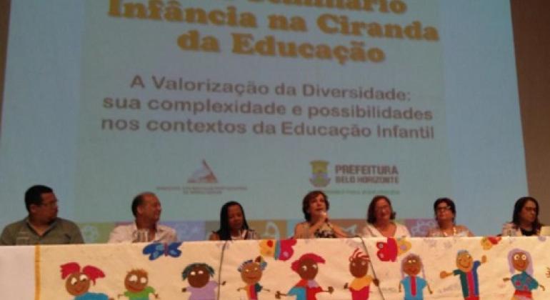 Secretária Municipal de Educação, Ângela Dalben, em mesa com professores da Rede Municipal de Ensino. Ao fundo, tela com o texto "XX Seminário Infância na Ciranda da Educação - A Valorização da Diversidade: sua complexidade e possibilidades nos contextos da educação Infantil".