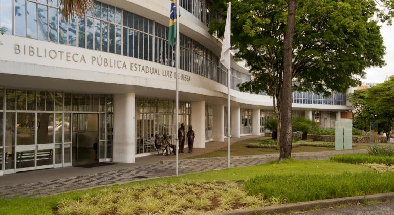 Foto da entrada da prefeitura. Tem uma árvore, um canteiro gramado na frente da biblioteca. 