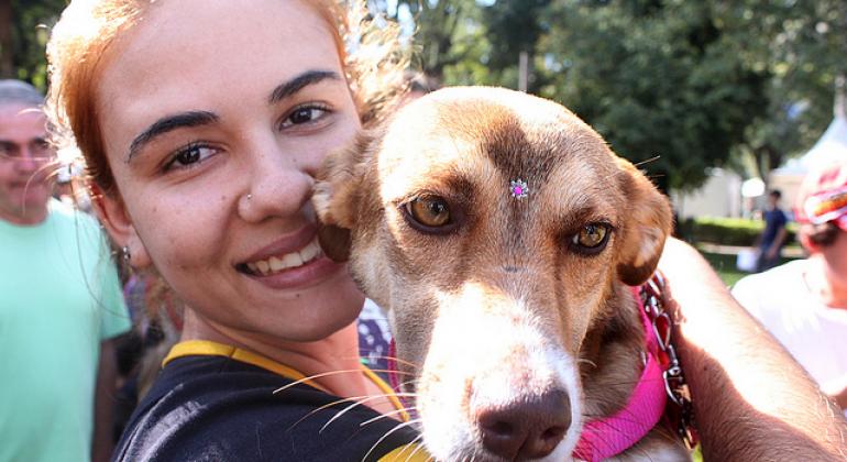 Jovem mulher segura um cão adotado com uma florzinha decorativa na testa.