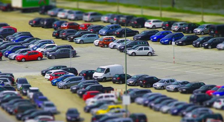 Mas de 40 carros estacionados em pátio durante o dia.