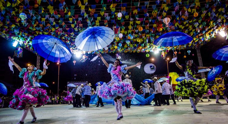 Meninas com vestidos coloridos de quadrilha levantando guarda-chuvas azuis. 