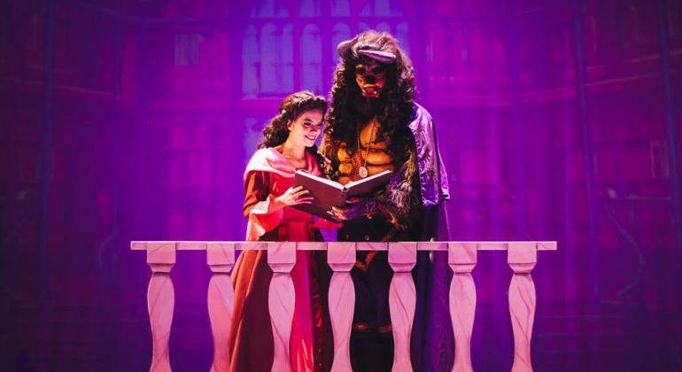 Teatro Francisco Nunes recebe musical “A Bela e a Fera". Foto: Daniel Augusto Bela, jovem com trajes de princesa, lê livro junto à Fera em uma sacada em cena teatral.