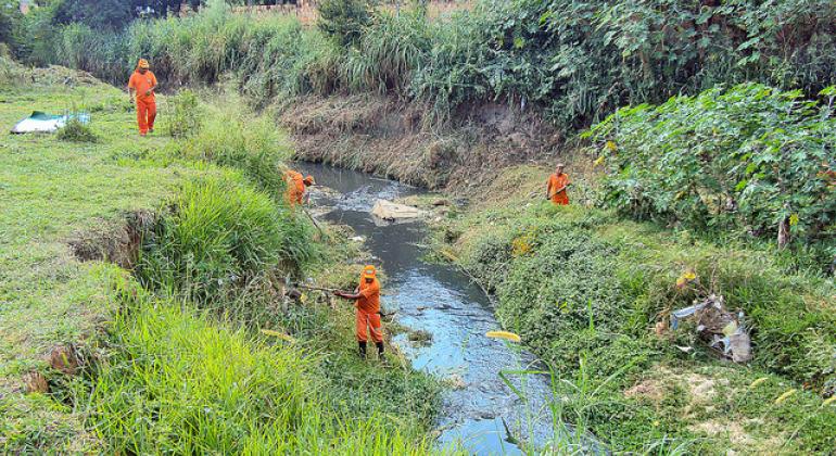 Quatro funcionários da Superintendência de Limpeza Urbana fazem limpeza do Córrego de Capão