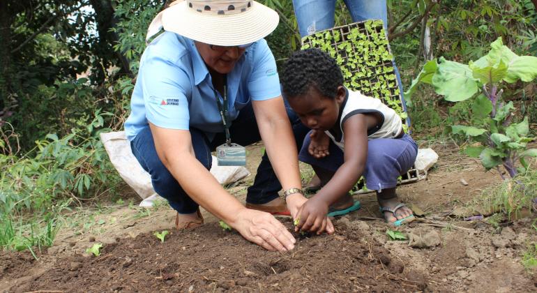 Técnica da Emater ensina criança a plantar mudas no solo durante o dia. 