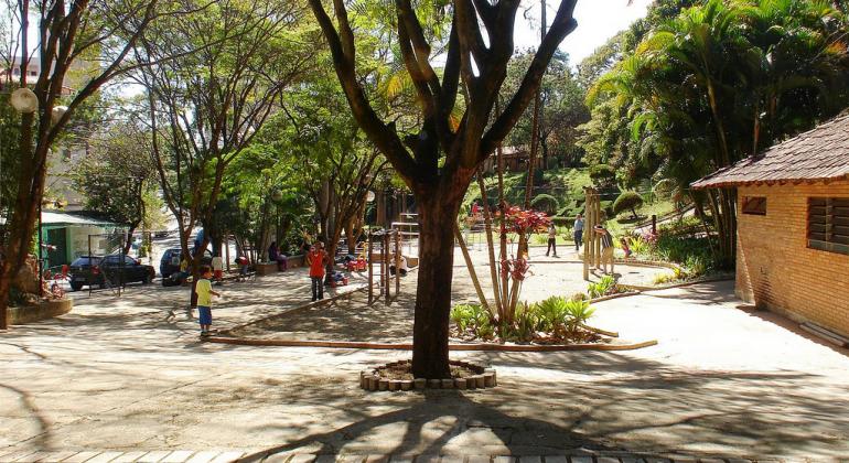 Parque com árvores e aparelhos de ginástica, grama e passeios durante o dia.