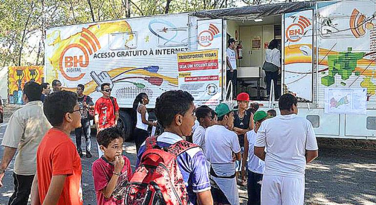 Cerca de dez alunos fazem fila para ter acesso ao Telecentro Móvel, que dá acesso a internet, durante o dia. Outros dois cidadãos estão ao redor do veículo. 