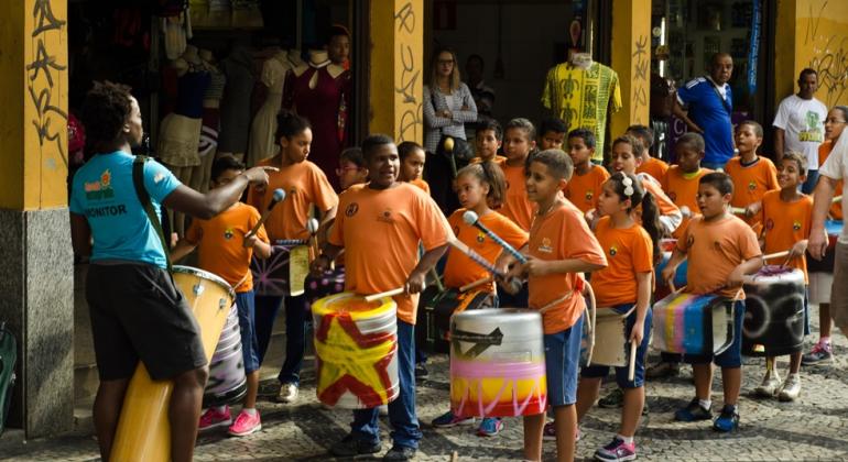 Semana das Mães foi comemorada no Shopping Popular Caetés Crianças com camisetas cor laranja com instrumentos de percussão em frente à entrada Shopping Caetés