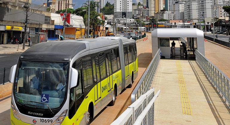 Pista do Move na Avenida Cristiano Machado com ônibus em movimento. Ao fundo, prédios.