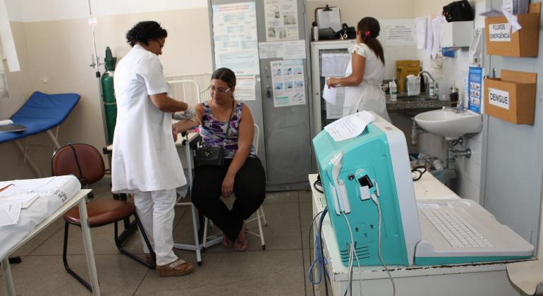 Enfermeira mede a pressão de paciente em laboratório do SUS