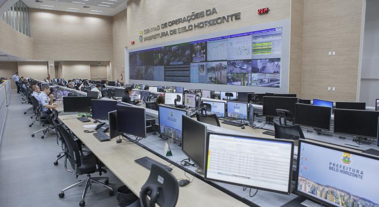 Sala principal do Centro de Operações da Prefeitura com computadores. Ao fundo, telão com câmeras que monitoram a cidade.