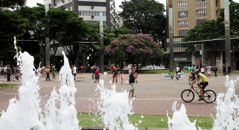 No primeiro plano, fonte da Savassi jorrando água. Logo atrás, belo-horizontinos ocupam a praça. Ao fundo, prédios do entorno da praça. 