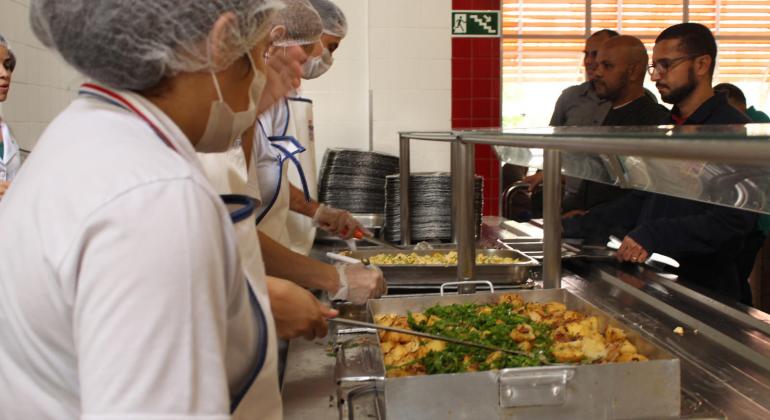 Na imagem, aparecem funcionários do Restaurante popular de costas servido refeição aos cidadãos.