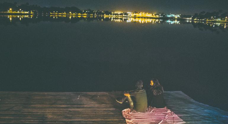 Casal sentado em deck de madeira de frente para a Lagoa da Pampulha