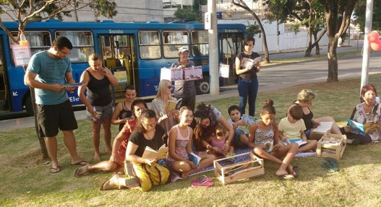 Literatura na Praça - Foto: Cida Lima/PBH Cerca de 20 pessoas, entre crianças e adultos, sentados no gramado lendo.
