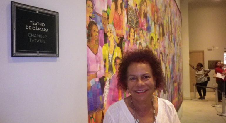 Dona Arlete sorri para foto em frente a quadro de obra de arte