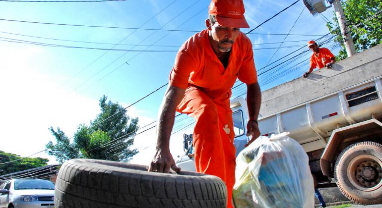 Prefeitura renegocia contratos de limpeza urbana - Foto: Divino Advincula/PBH Gari faz coleta de lixo. Em uma das mãos segura um pneu, em outra uma sacola.