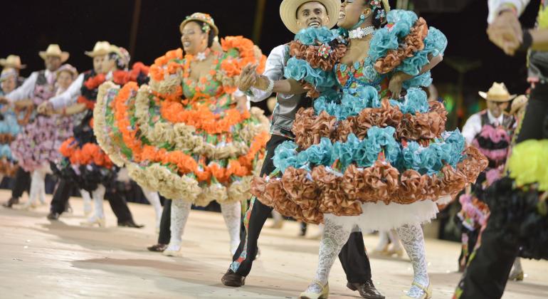 Pessoas usando vestidos coloridos e dançando festa junina.