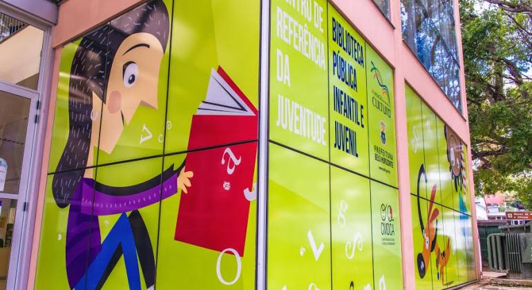 Detalhe da entrada da Biblioteca Pública Infantil e Juvenil de Belo Horizonte, no Centro de Referência da Juventude. No desenho colorido do viro, garota sorri e abre um livro.