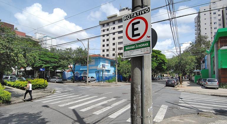 Foto: Divino Advincula Cruzamento de trânsito com placa de Estacionamento Rotativo em uma das esquinas, durante o dia.