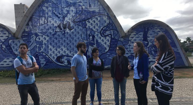 Grupo de cinco voluntários internacionais da PBH em frente ao painel de Portinari na Igreja de São Francisco, na Pampulha.