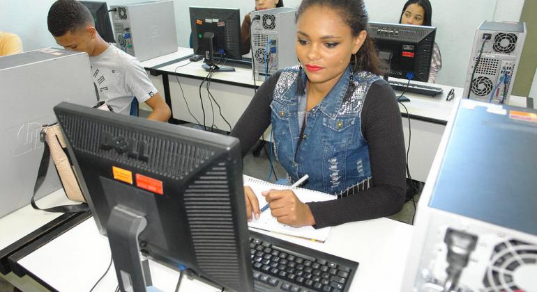 A jovem Kelimara sentada, em frente a um computador, ao fundo, outros três colegas também em frente ao computador.