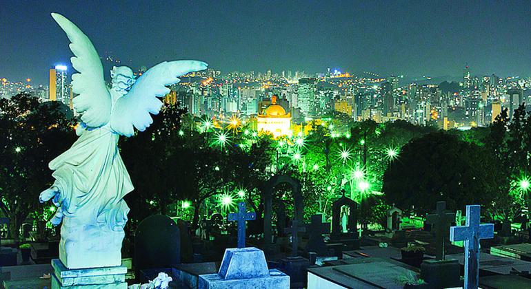 A partir do dia 17 de julho, o Cemitério do Bonfim olta a receber velórios noturnos, que estavam suspensos há pouco mais de um ano. Foto: Pierre Bonnereau Cemitério do Bonfim à noite com Anjo de sepultura de constas em primeiro plano. Ao fundo, cidade iluminada.