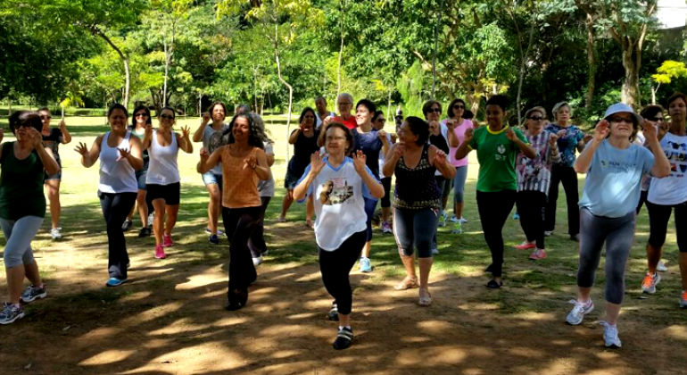 Cerc de onze pessoas praticando dança chinesa rejuvenescedora em local com muito verde no Buritis