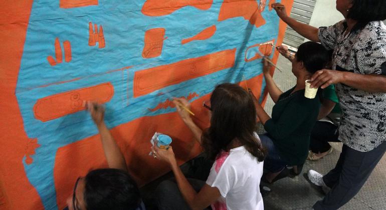 Quatro pessoas pintam mural na parede, atividade faz parte de oficina de artes da Escola Livre de Artes.