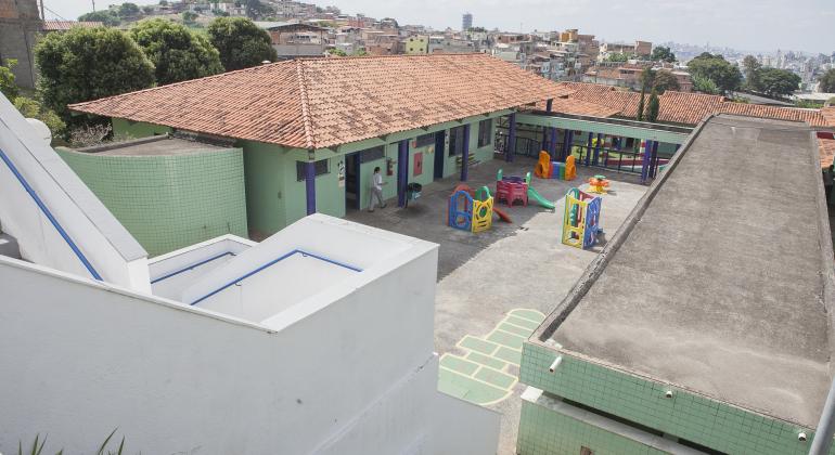 Pátio de escola municipal com brinquedos infantis coloridos.