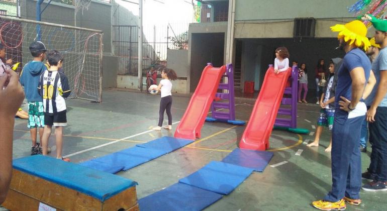 Crianças brincam no escorregador acompanhadas por monitores, atividades fazem parte do programa Escola nas Férias. 