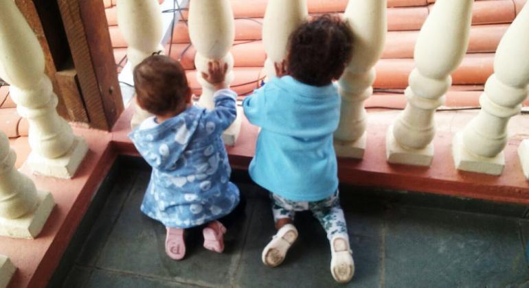 Foto: Divulgação/PBH Duas crianças com menos de 2 anos na varanda de uma casa.