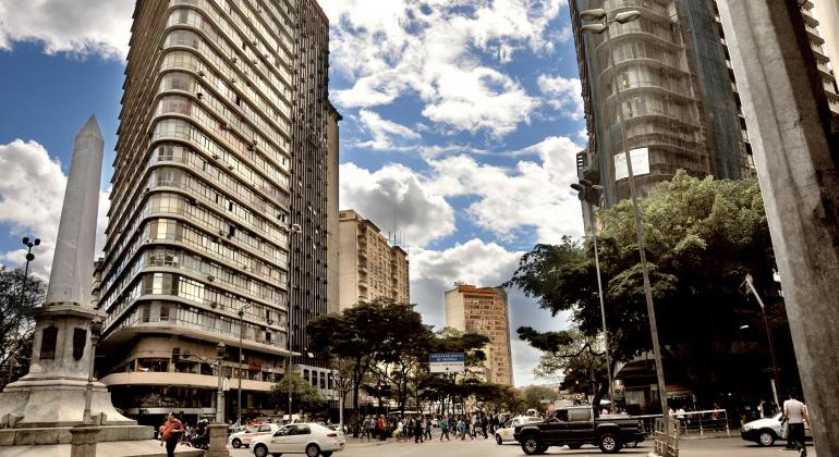 Pessoas e carros transitam na Praça Sete durante o dia. 