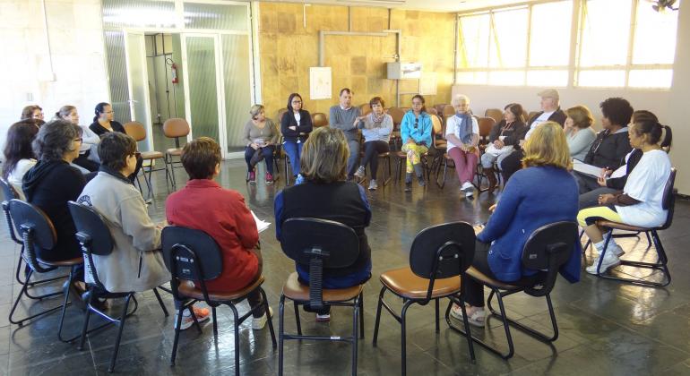 Quinze pessoas se reúnem em círculo, dinâmica do projeto Roda de Conversa que permite a troca de experiências.