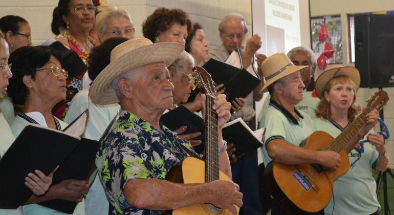 Grupo de mais de dez idosos canta e toca instrumentos no CAC Barreiro. 