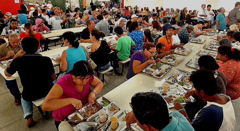 Confira os cardápios dos Restaurantes Populares de 17 a 21 de julho. Cidadãos comendo em restaurante popular durante o dia.