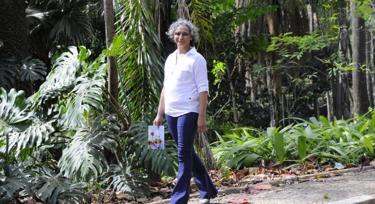 A escritora e servidora da Prefeitura, Soraia Evangelista, caminha pelo parque municipal segurando seu livro "Um câncer, uma felicidade..."