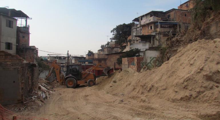 BH em Pauta: Vila Cabana Pai Tomaz recebe obra urbanizadora Trator trabalha em obra na Vila Cabana Pai Tomaz. À direita, há barracos. Ao fundo, céu azul.