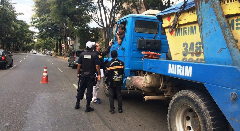 Dois fiscais da Prefeitura abordam caminhão que transporta resíduos para em blitz educativa.