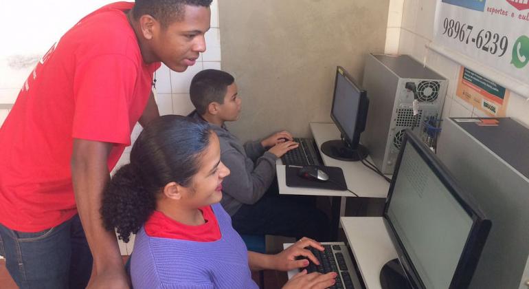 Voltado às comunidades, projeto de capacitação tecnológica desenvolvido pela Prodabel inicia a segunda fase. Foto: Prodabel/PBH Monitor da Prodabel auxilia dois jovens em atividades de informática.