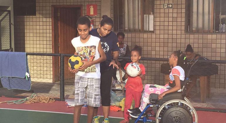 Quatro crianças reunidas para a prática esportiva: uma delas é cadeirante e outras duas estão com bola nas mãos.