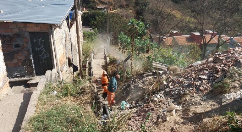 Dois agentes realizam limpeza de escadaria ao lado de morro da Vila Cemig.