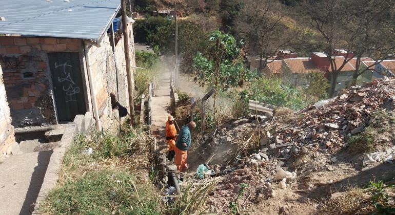 Limpeza, campanha educativa e visitas domiciliares marcam ações integradas em comunidades na região do Barreiro. Foto: Cláudio Passos/PBH Dois agentes realizam limpeza de escadaria ao lado de morro da Vila Cemig.