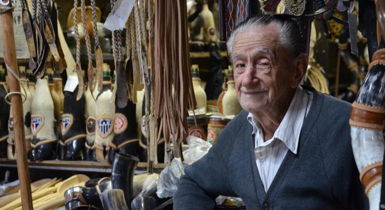 À frente de loja com chicote de couro, berrante e outros acessóros rurais, senhor de idade.