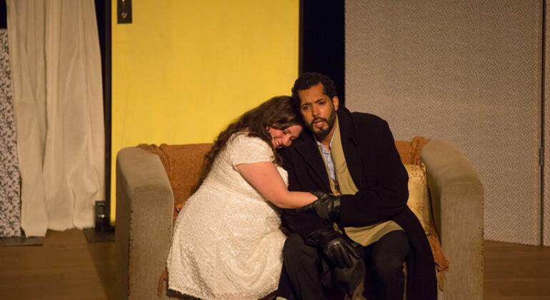 O Segredo de Susanna - Cia Mineira de Ópera Casal se abraça sentado em sofá; cena do espetáculo "O Segredo de Susanna", da Cia Mineira de Ópera