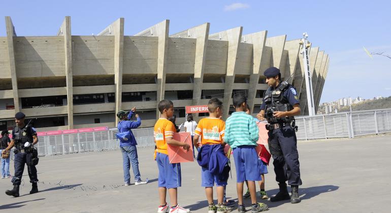 Cerca de quatro crianças são auxiliadas por guarda municipal sobre como soltar pipa de maneira segura na área externa do Mineirão.