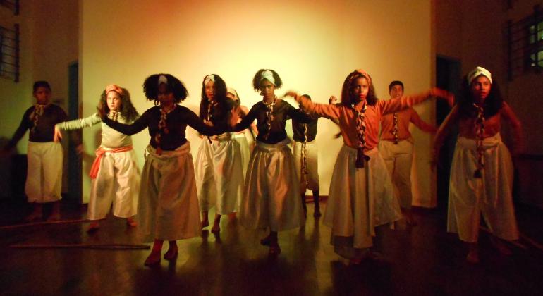 A partir do teatro, projeto em centro cultural da região Leste de BH mobiliza a comunidade em torno da valorização da cultura negra. Foto: Marcia Cristina Dez dançarinos, dos quais três são homens, fazendo passos de dança afro.